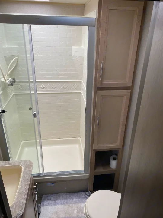 RV rental bathroom: compact space featuring a glass-enclosed shower, sink, toilet, and built-in storage cabinets.. Coachmen Catalina 2021