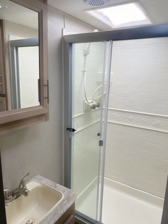 Clean RV rental bathroom featuring a sink, vanity, mirror, and a shower with glass doors and a skylight.. Coachmen Catalina 2021