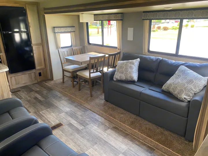 Cozy RV rental living space: dark sofa with pillows, wooden dining table & chairs, fridge, and wood flooring.. Coachmen Catalina 2021