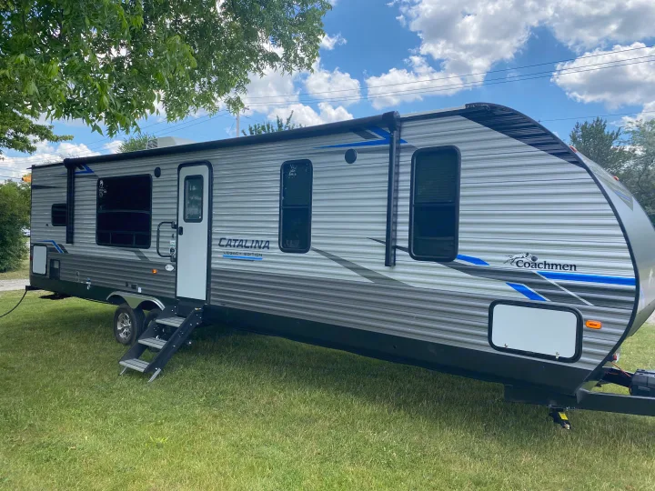 Gray Coachmen Catalina travel trailer for rv rental, parked on grass. Shows side with steps, windows, and extended awning.. Coachmen Catalina 2021