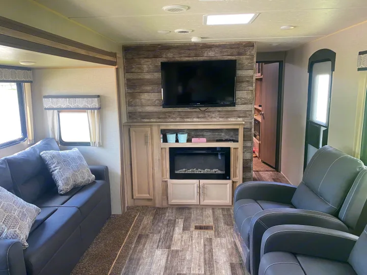 Cozy RV rental living room features a modern fireplace, TV, comfortable recliners, and a sofa for relaxing road trips.. Coachmen Catalina 2021