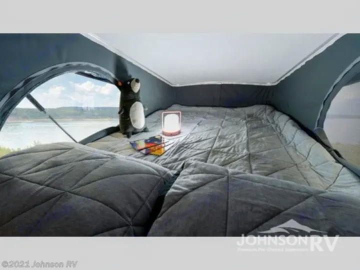 Experience the comfort of an RV rental: a cozy bedroom with quilted bedding, lamp, plush toy, and a beautiful waterside view.. Winnebago Solis 2022
