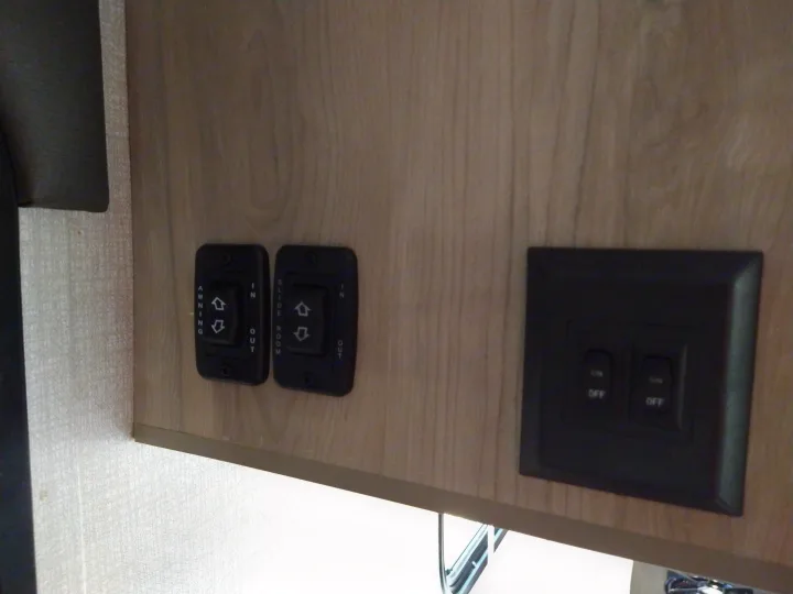 RV rental control panel: Awning, slide room, and power switches on a wood-grained surface.. KZ 181BH 2021