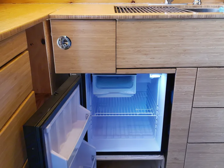 RV rental: Bamboo kitchen counter, sink, open illuminated mini-fridge, and cabinets with a round latch.. Mercedes Sprinter 2006