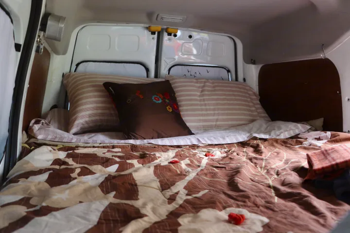 Comfortable bed inside an RV rental, featuring striped pillows and a brown patterned comforter for a cozy rest.. Ford Connect 2012