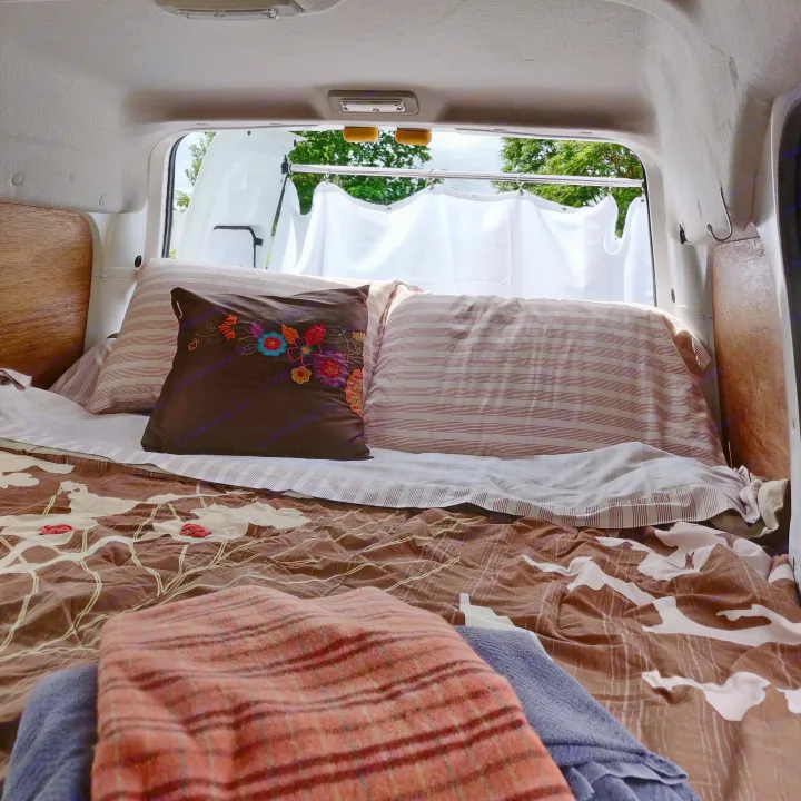 Inside a cozy RV rental: a comfortable bed with colorful pillows, offering a scenic view out the window.. Ford Connect 2012