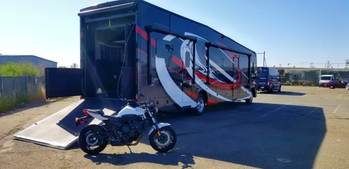 An impressive black and red RV rental, a toy hauler with an extended ramp, ready for a white motorcycle to load up.. Thor Outlaw 2020