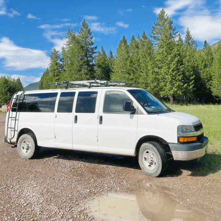 White camper van with a roof rack and ladder on a gravel road, parked by a mud puddle and forest. Perfect for an rv rental.. Chevrolet Express 2007