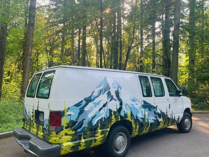 White RV rental van with a custom mountain & forest mural, parked in a sun-dappled woods. Ideal for nature exploration.. Ford Econoline E250supercab 2006