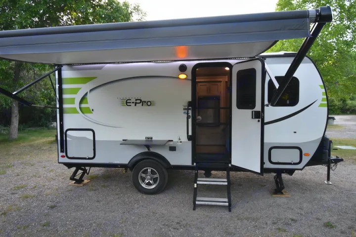 A white & green Flagstaff E-Pro rv rental with an extended awning, open door, and stairs, parked on a gravel campsite.. Forest River Flagstaff E-Pro 2019