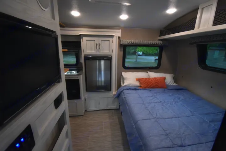 Cozy RV rental interior featuring a bedroom area, small kitchen with a refrigerator, and a mounted flat-screen TV.. Forest River Flagstaff E-Pro 2019