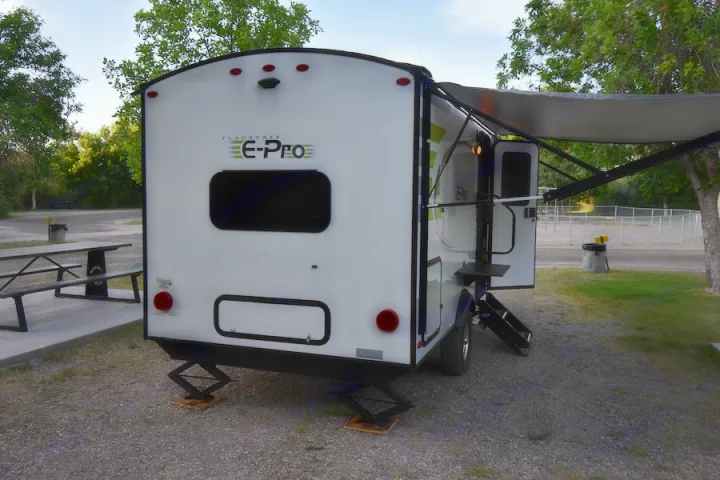 White Flagstaff E-Pro RV rental travel trailer at a gravel campsite. Awning extended, jacks down, ready for camping.. Forest River Flagstaff E-Pro 2019