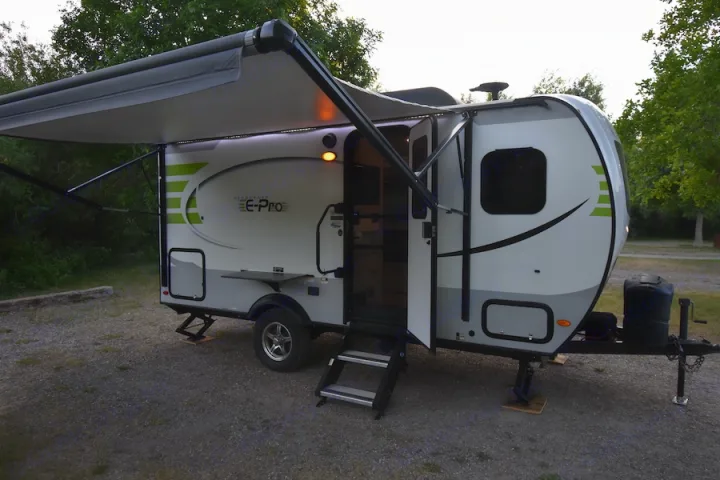This Flagstaff E-Pro travel trailer RV rental is set up at a campsite with its awning extended and door open, perfect for camping.. Forest River Flagstaff E-Pro 2019
