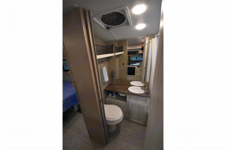 RV rental: Compact interior shows a bathroom with dual sinks, toilet, and overhead fan. A blue bed is visible left.. Forest River Flagstaff E-Pro 2019