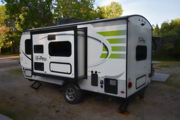 A white Flagstaff E-Pro travel trailer, parked on gravel at a campsite with its slide-out extended, perfect for an RV rental.. Forest River Flagstaff E-Pro 2019