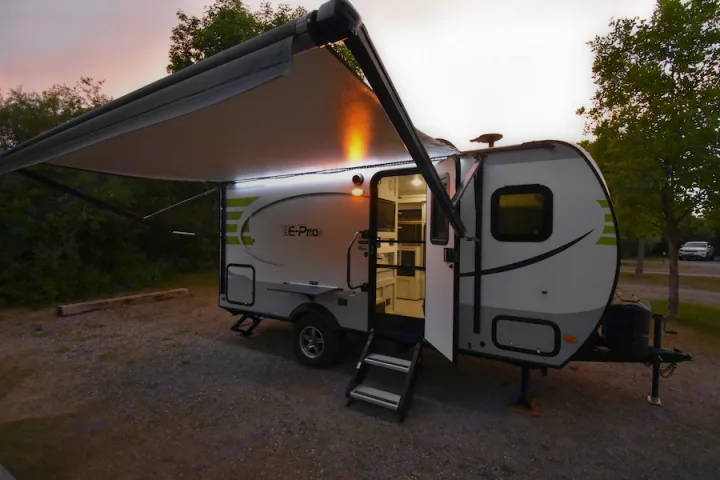 This E-Pro travel trailer (rv rental) is illuminated at dusk in a campsite, with its awning extended and door open, ready for camping.. Forest River Flagstaff E-Pro 2019