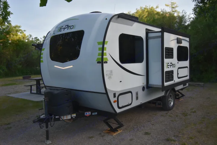 A white and gray E-Pro travel trailer, perfect for an rv rental, is parked at a campsite with its slide-out open.. Forest River Flagstaff E-Pro 2019