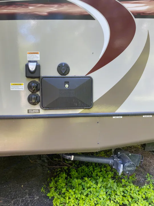 An RV rental's utility panel features electrical, city water, shower, and black/grey tank waste connections, with warning labels.. Coleman Light 2405BH 2017
