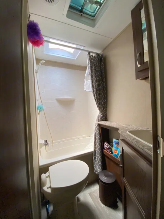 Clean, compact RV rental bathroom with shower-tub, toilet, sink vanity, and stylish curtain. Ideal for on-the-road comfort.. Coleman Light 2405BH 2017