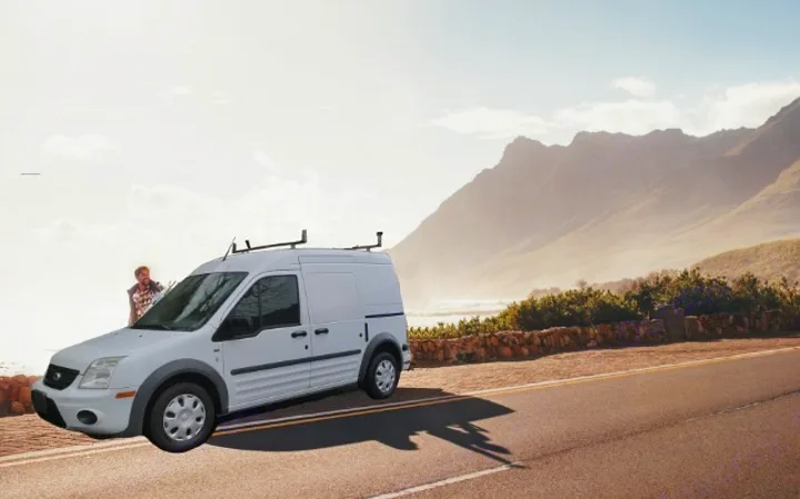 White van with man on scenic coastal road by mountains & ocean. Perfect for your RV rental adventure!. Ford Connect 2012