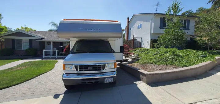 White Fleetwood RV parked in a paved driveway on a sunny day, ready for RV rental. Homes and greenery surround it.. Fleetwood Jamboree 2006