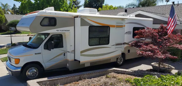 A white Fleetwood Class C rv rental with an extended slide-out, parked in a sunny residential driveway.. Fleetwood Jamboree 2006