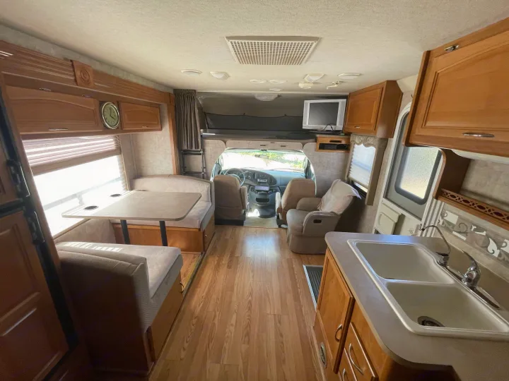 View of an RV rental interior showing a dinette, kitchen, cockpit, and cab-over bed.. Fleetwood Jamboree 2006