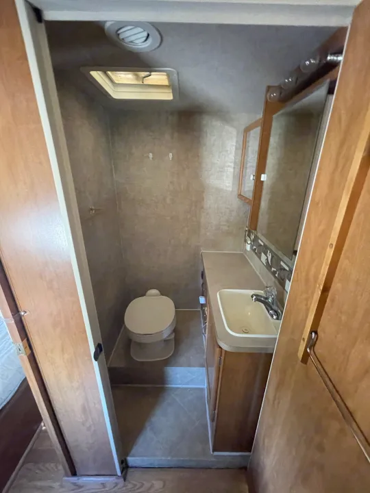 Compact RV rental bathroom featuring a toilet, sink with vanity, mirror, and overhead skylight for natural light.. Fleetwood Jamboree 2006