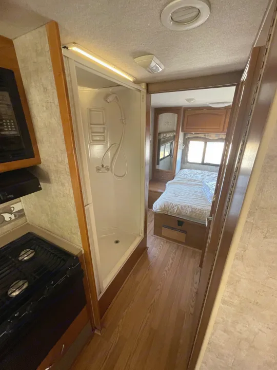 Interior of an RV rental: A compact layout with a kitchen area (stovetop, microwave), a stand-up shower, and a rear bedroom with a bed.. Fleetwood Jamboree 2006