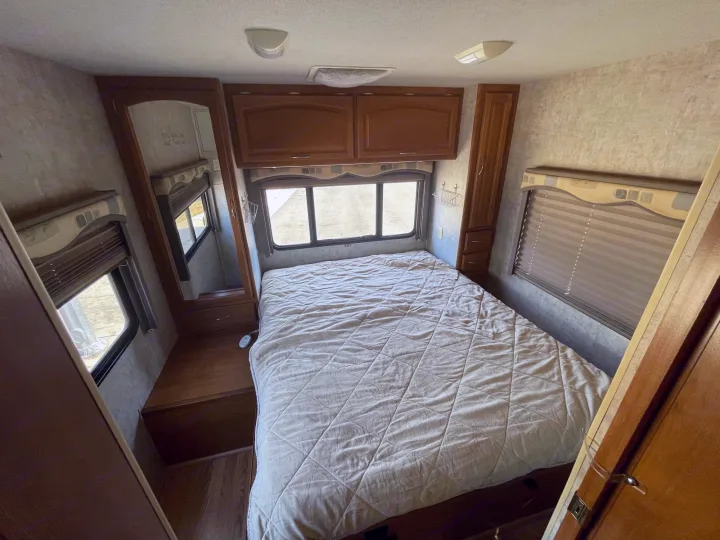 RV rental bedroom: a cozy space with a large bed, overhead storage, and natural light from windows.. Fleetwood Jamboree 2006