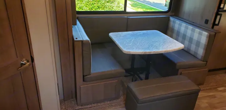 Cozy RV rental dinette with U-shaped booth seating, a marble-look table, and plaid accents for comfortable meals.. Grand Design 2400BH 2022