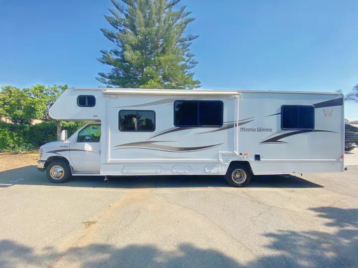 White "Minnie Winnie" RV ready for your next rv rental adventure, parked on asphalt under a clear blue sky.. Winnebago Minnie Winnie 2015