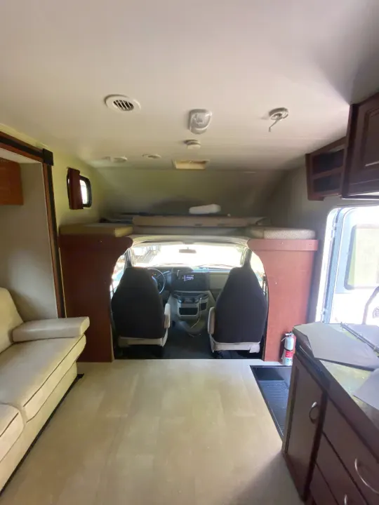 Inside an RV rental: a spacious interior showing the living area, kitchen, cab, & over-cab bunk, from rear to front.. Winnebago Minnie Winnie 2015
