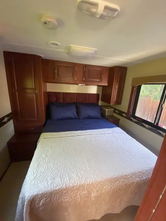 RV rental: a cozy bedroom featuring a large bed with blue linens, wood storage, and an emergency exit window.. Winnebago Minnie Winnie 2015