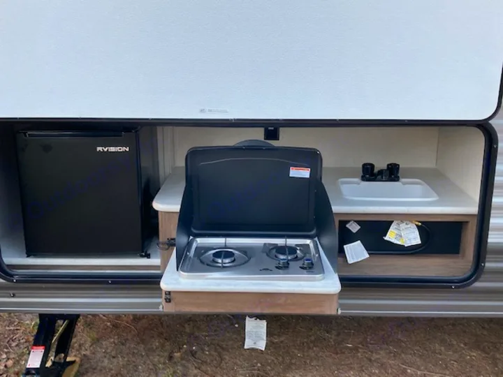 An RV rental's outdoor kitchen featuring a black mini-fridge, two-burner stove, and white sink for camping.. Forest River Prime Time Avenger 2021