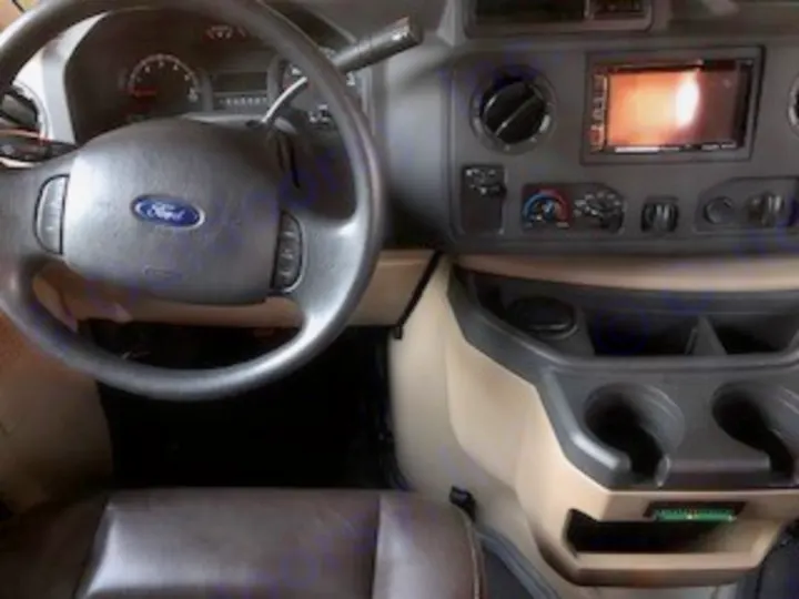 RV rental cockpit interior. Ford steering wheel, dashboard, infotainment, climate controls, cupholders. Spacious driver's area with brown seats.. Forest River Other 2017