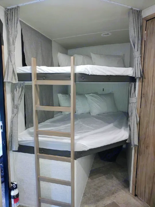 Cozy RV rental features bright, made-up bunk beds with a ladder, providing comfortable sleeping arrangements within a compact space.. Palomino Solaire 243bhs 2021