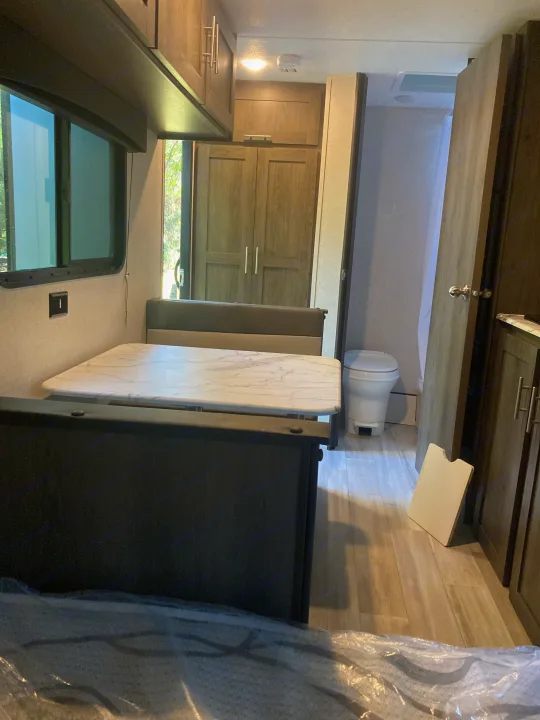 Inside an RV rental: features a dinette with bench seating, overhead cabinets, and a visible bathroom setup.. Other 1906st Saga 2021