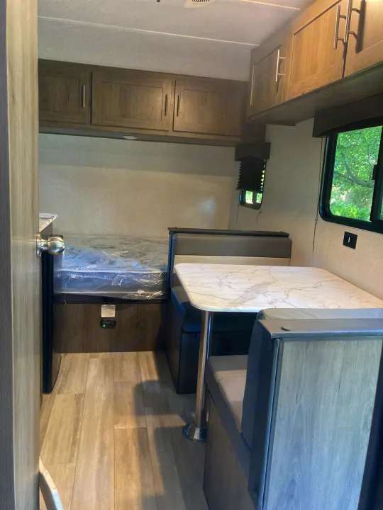 Inside an RV rental: a compact interior featuring a bed, dinette with marble-look table, and wood cabinets.. Other 1906st Saga 2021