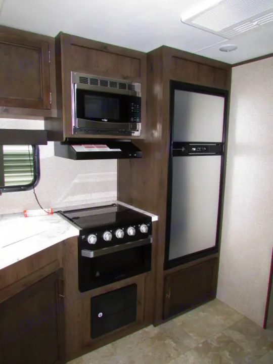 RV rental kitchen featuring stainless microwave, fridge, & Furrion range. Compact, well-equipped space.. Jayco Jay Flight SLX 2021