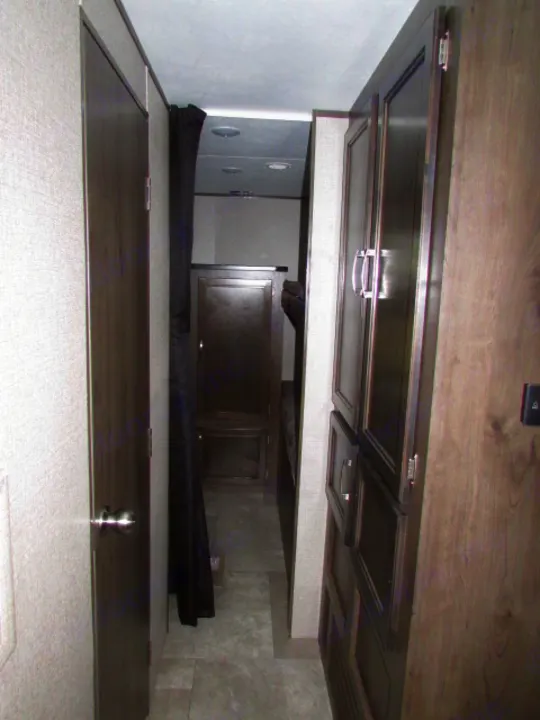 This RV rental interior shows a narrow hallway with a door, dark privacy curtain for a bunk area, and storage cabinets.. Jayco Jay Flight SLX 2021