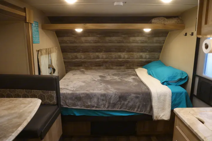 Step into this cozy RV rental's interior bedroom, featuring a plush bed, wood accent wall, and "Camping Rules" sign, plus a dinette.. Coachmen Catalina 2021