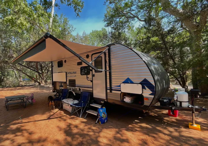 This RV rental is perfectly set up for camping under shady trees, with a picnic table, chairs, and a dog ready for outdoor adventures.. Coachmen Catalina 2021