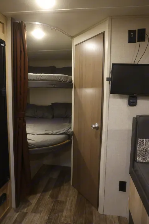 Cozy rv rental interior featuring a bunk bed area with privacy curtains, a door, and a wall-mounted TV, showcasing compact travel living.. Coachmen Catalina 2021