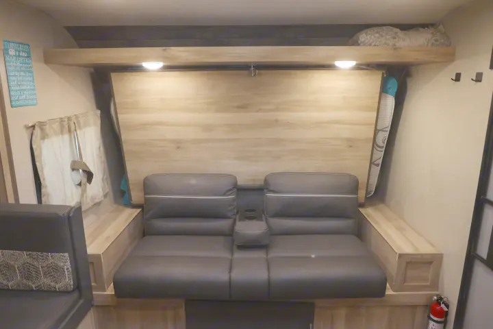 Cozy RV rental interior with dark seating, a folded wall bed, overhead shelf, and 'Camping Rules' sign, perfect for relaxation.. Coachmen Catalina 2021
