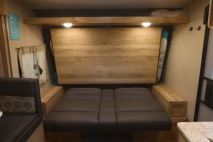 RV rental interior showcasing a converted dinette bed with comfortable cushions, overhead lights, and a fun 'Camping Rules' sign.. Coachmen Catalina 2021