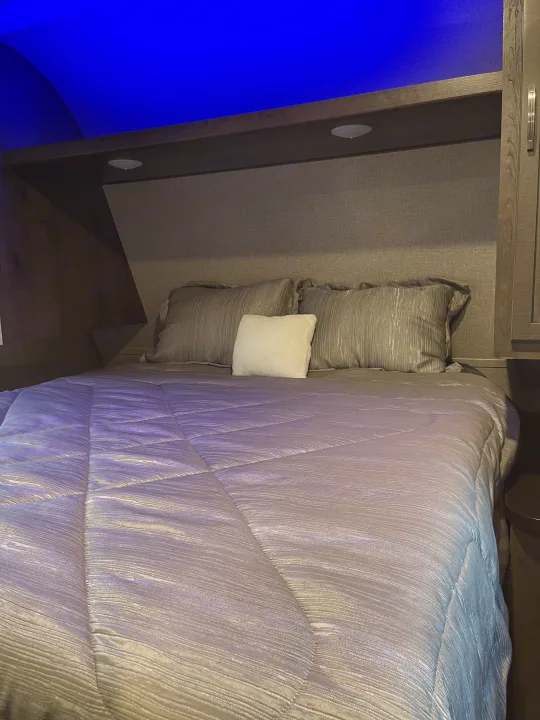 Cozy RV rental bedroom featuring a made bed with gray bedding, blue mood lighting, and built-in storage.. Jayco Jay Flight 2020