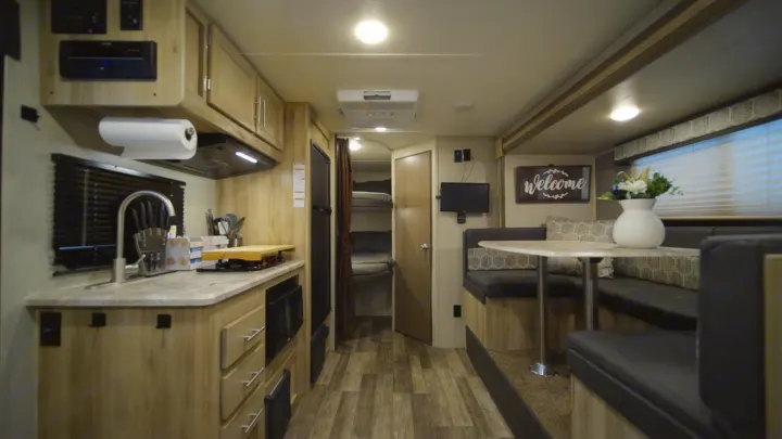 RV rental interior with a compact kitchen, dinette seating, and bunk beds in the background.. Coachmen Catalina 2021
