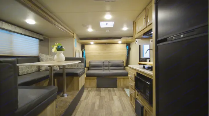 RV rental interior view: compact living space with a dinette, kitchen, and sofa bed. Features wood-look flooring and light wood cabinets.. Coachmen Catalina 2021