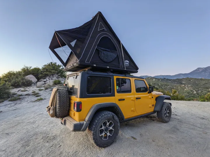 Yellow Jeep Wrangler with an open rooftop tent, ideal for an **rv rental** adventure amidst scenic mountains.. Jeep Wrangler Unlimited Rubicon 2020